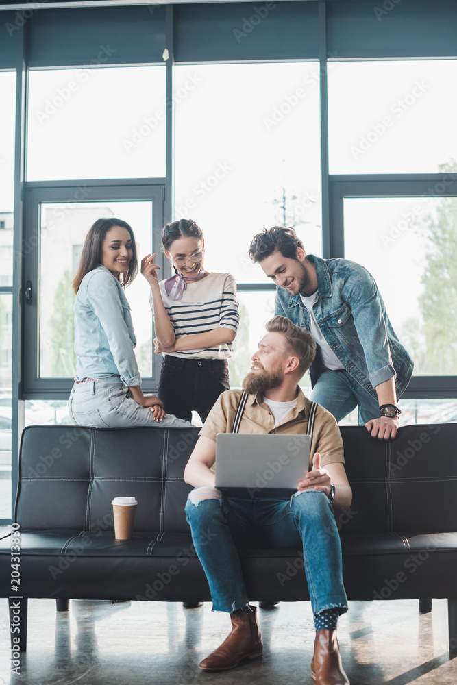 Businessman and women looking at their male colleague working on laptop in modern office Businessman and women looking at their male colleague working on laptop in modern office