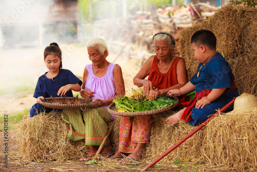 Foto Traditional Asian Thai rural daily life, grandchildren in cultural costumes help their seniors preparing local food ingredients for the meal