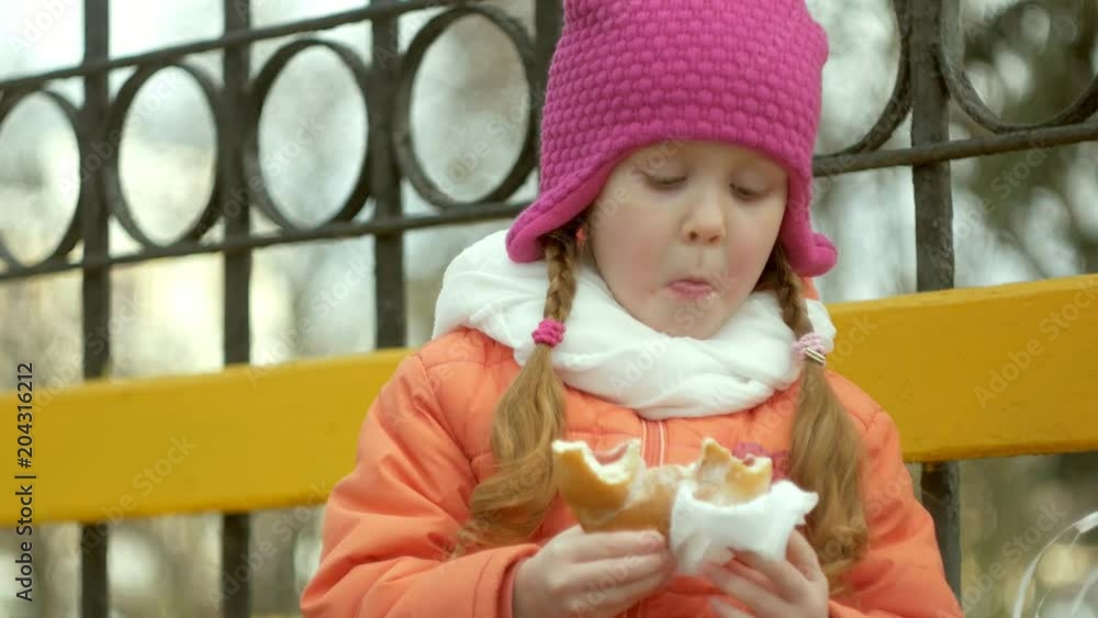 Beautiful girl sits on a park bench and eats a delicious dessert Beautiful girl sits on a park bench and eats a delicious dessert