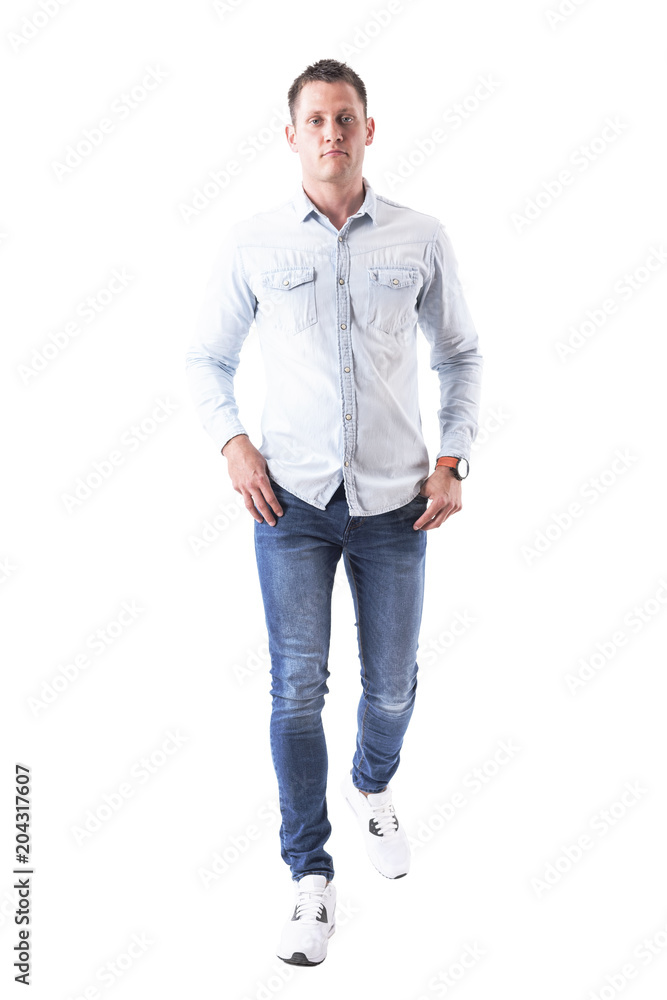 Fototapeta premium Content serious young successful man walking with hands in pockets looking at camera. Full body isolated on white background. 
