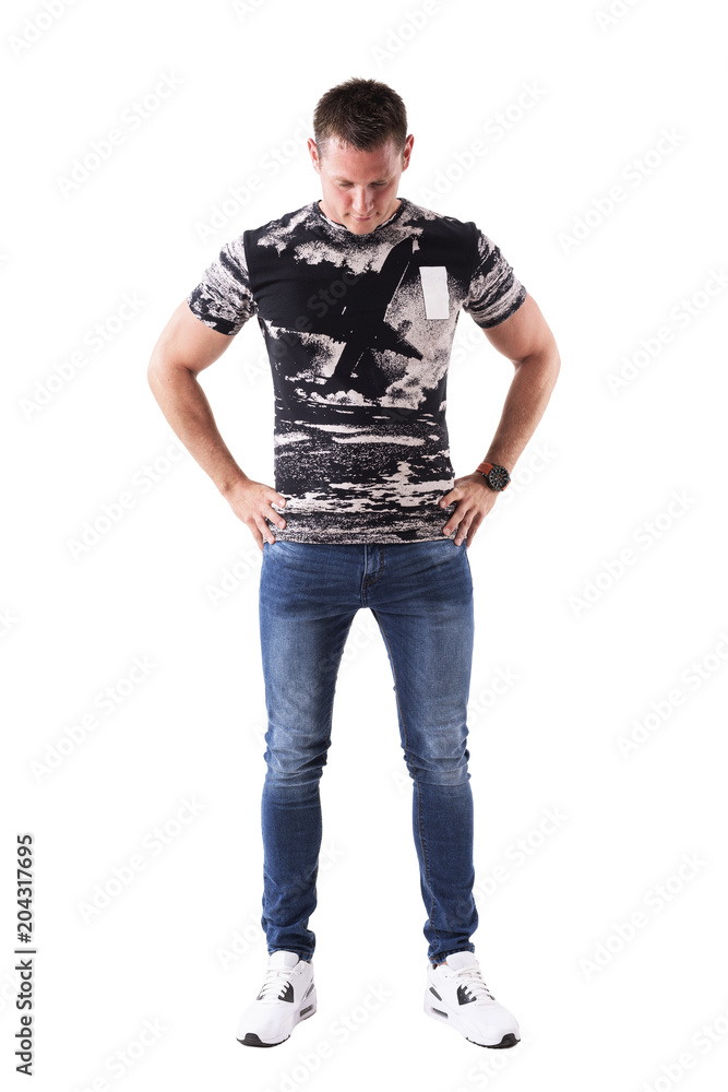 Serious young adult casual man with hands on hips looking down thinking. Front view. Full body isolated on white background. Serious young adult casual man with hands on hips looking down thinking. Front view. Full body isolated on white background.