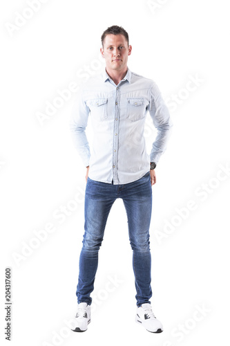Content man in light blue shirt and jeans looking at camera with hands in back pockets. Full body isolated on white background. 