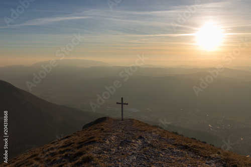 Cross on top of Mt. Serrasanta (Umbria, Italy), with warm golden hour colors and sun low on the horizon