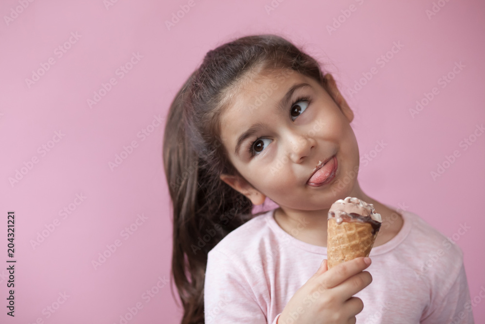 Happy smiling child girl eating ice cream. Pastel pink background. Happy smiling child girl eating ice cream. Pastel pink background.