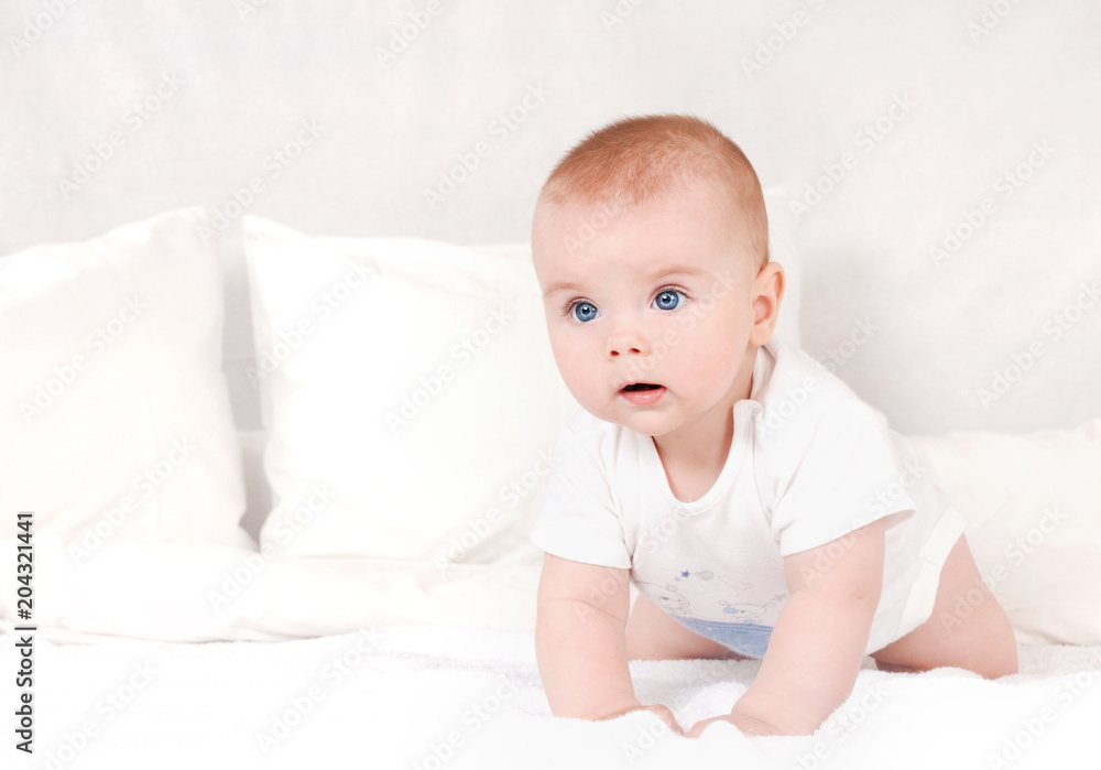 Portrait of sweet newborn infant crawlng on white bed serious looking away