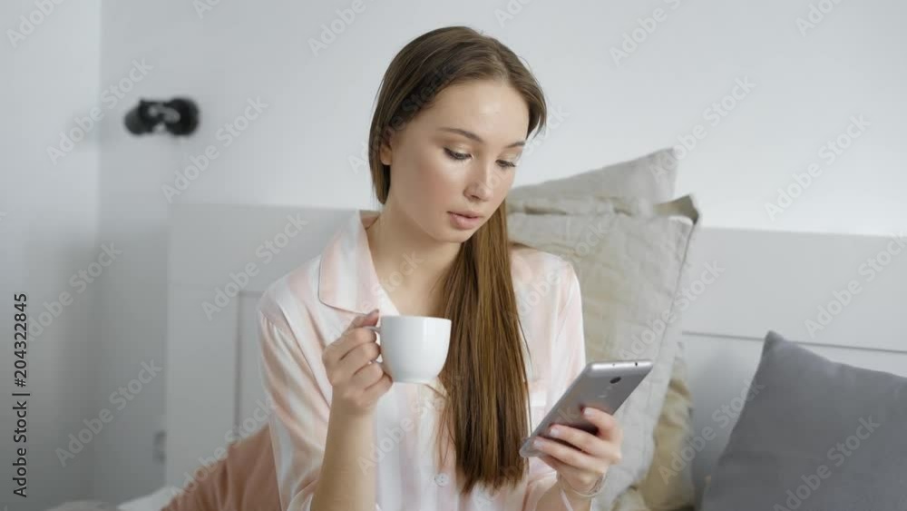 Close up portrait of a cute lovely brunette girl with a cup and smartphone in bedroom. Close up portrait of a cute lovely brunette girl with a cup and smartphone in bedroom.