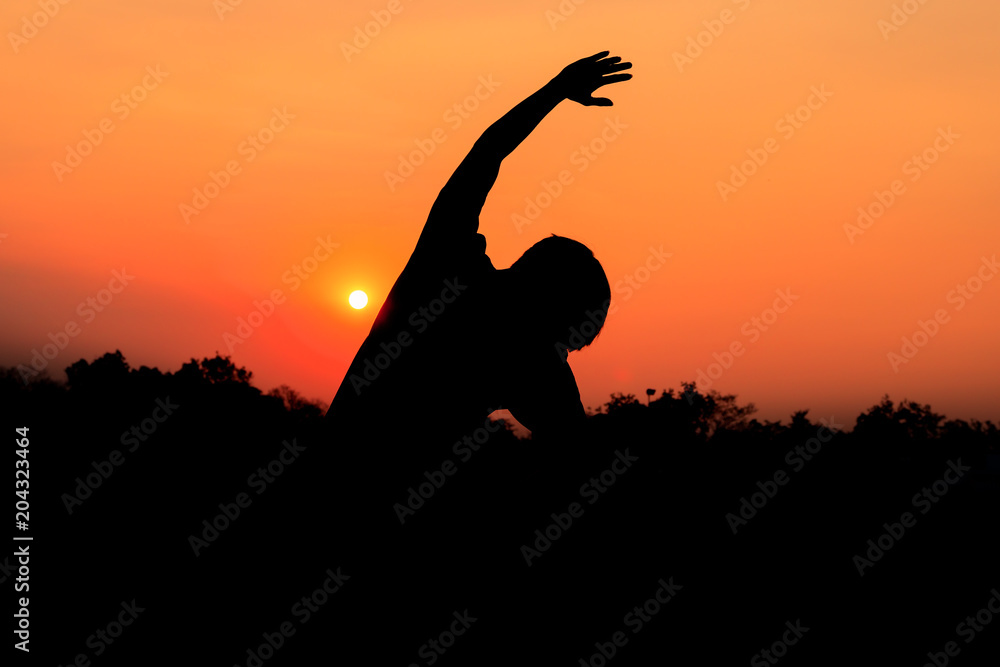 Silhouette of male meditating and yoga practicing with exercise at sunrise in public park morning