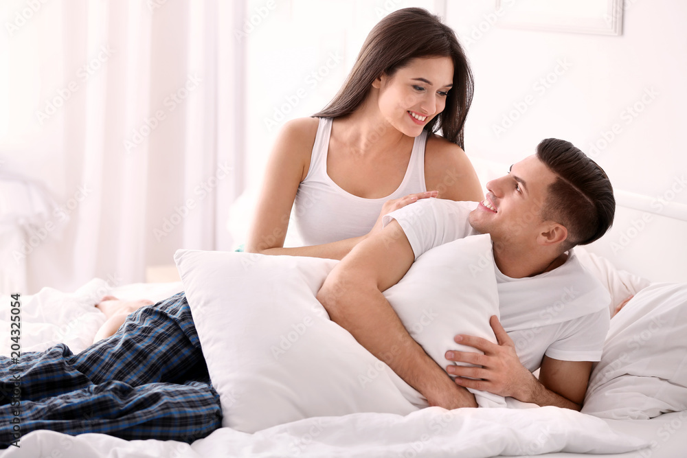 Fototapeta premium Young couple on bed with soft pillows at home