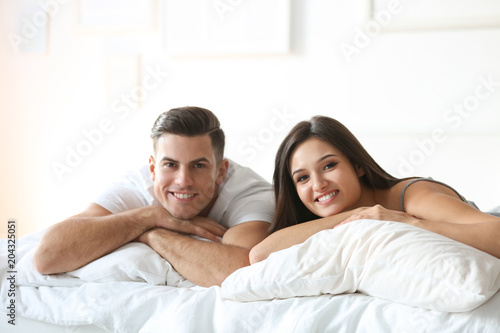 Young couple lying on bed with soft pillows at home