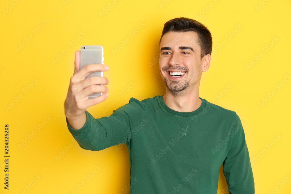 Young handsome man taking selfie against color background Young handsome man taking selfie against color background