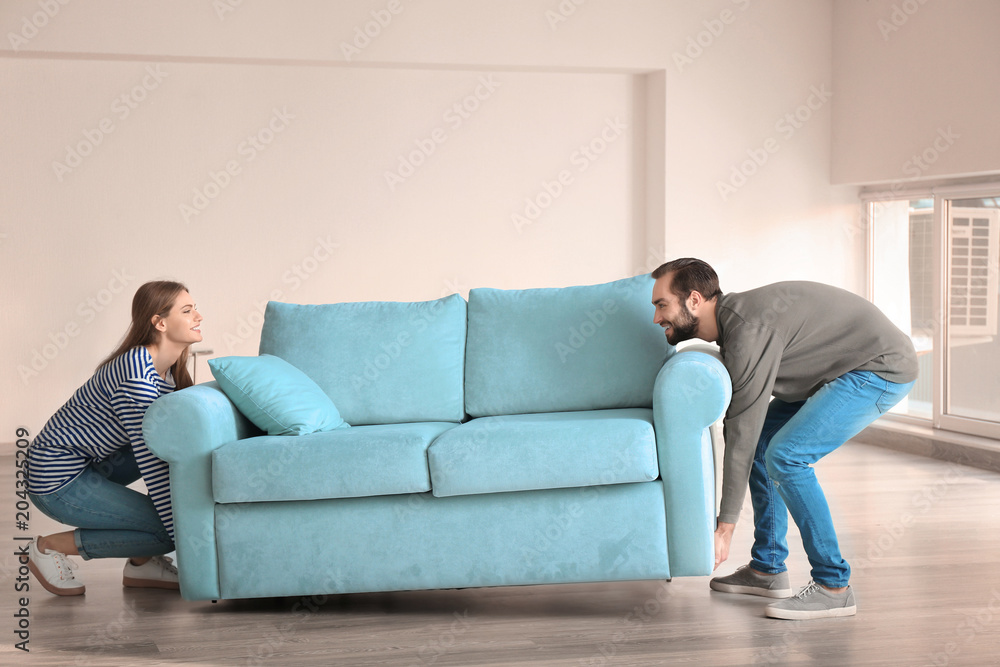 Young couple lifting sofa in empty room. Moving day