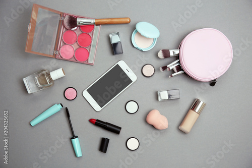 Flat lay composition with smartphone and makeup products for woman on grey background