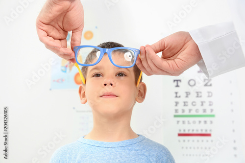 Fototapeta Naklejka Na Ścianę i Meble -  Male ophthalmologist putting glasses on  little boy in clinic