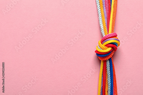Different ropes tied together with knot on color background. Unity concept photo