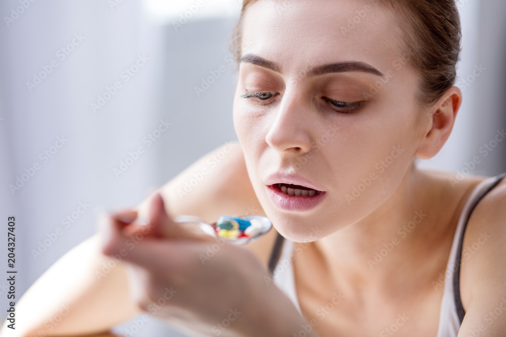 My medicine. Cheerless young woman holding a spoon while eating pills My medicine. Cheerless young woman holding a spoon while eating pills