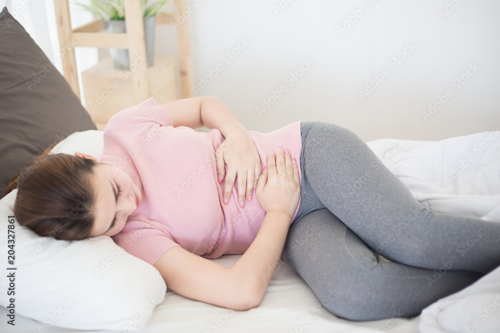 Young asian woman suffering from abdominal pain on the bed. Young asian woman suffering from abdominal pain on the bed.