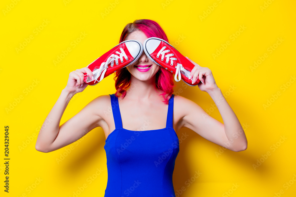Fototapeta premium Young pink hair girl in blue dress with gumshoes. Portrait isolated on yellow background