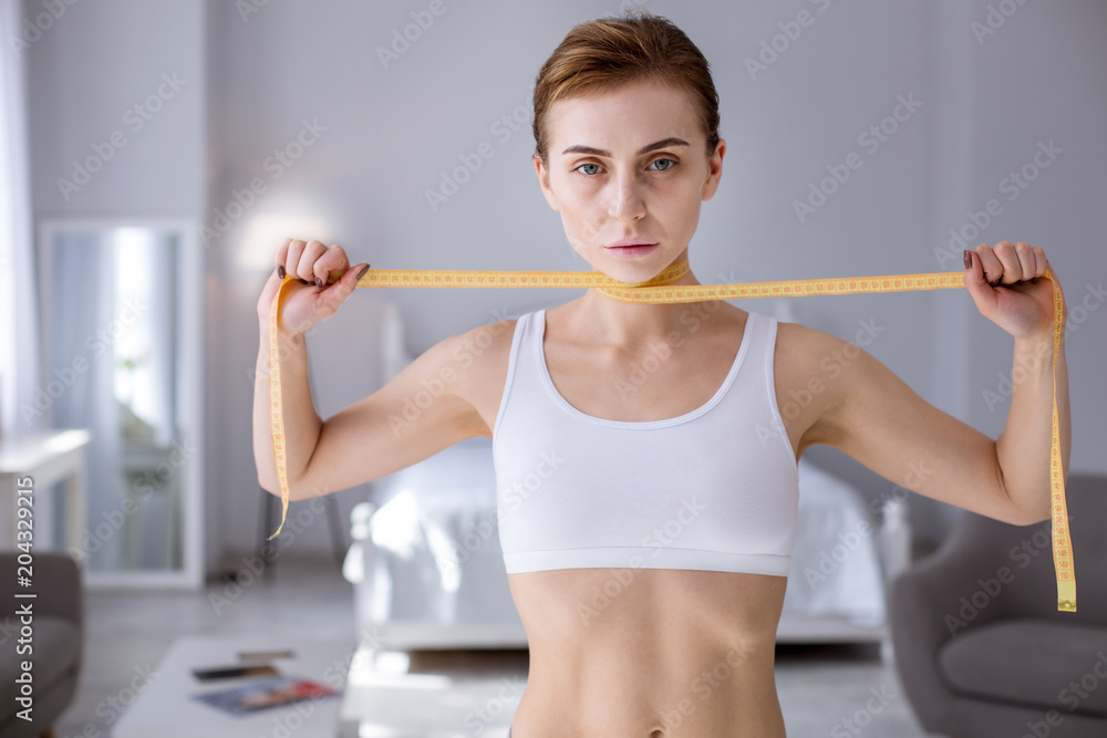 So exhausted. Pale young woman holding a centimetertape around her neck while looking at you