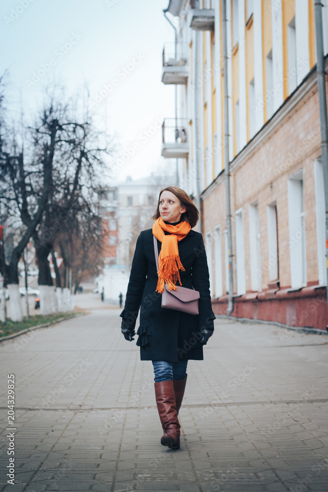Portrait of a young woman in a black coat and red scarf in the city
