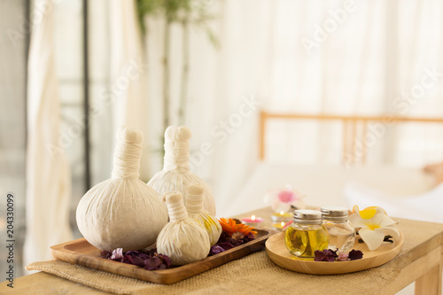 Selective focus of Herbal compress balls with oil on the wooden table in spa salon and blurred background of woman lying on bed. alternative medicine and relaxation Concept.