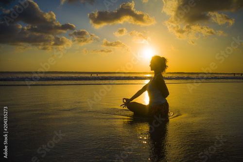 silhouette of young fit and attractive sport woman in beach sunset yoga practice workout sitting on wet sun in front of sea in meditation relaxation
