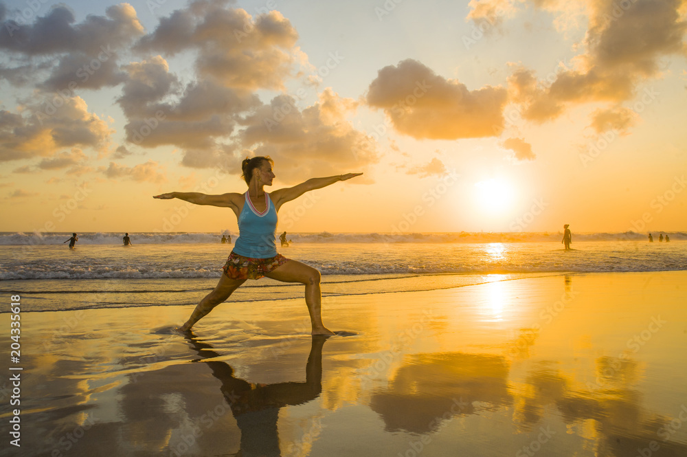 young fit and attractive sport woman in beach sunset yoga practice workout on wet sun in front of the sea in meditation and relaxation exercise