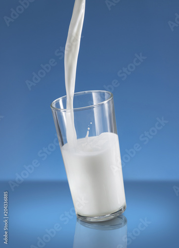 Pouring Milk Splash in A Glass Over Blue Background