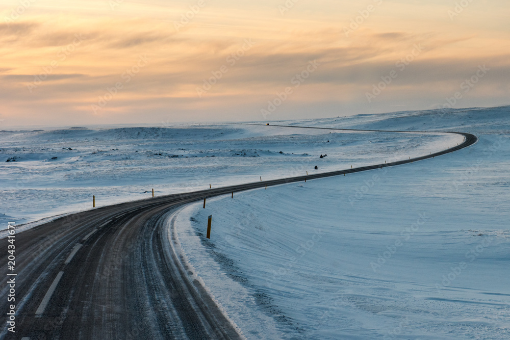 Winding road in snow fields at sunset