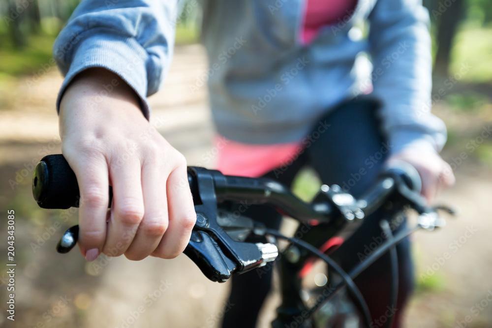 Woman riding a mountain bicycle along path at the forest. Closeup on handlebar with female hand