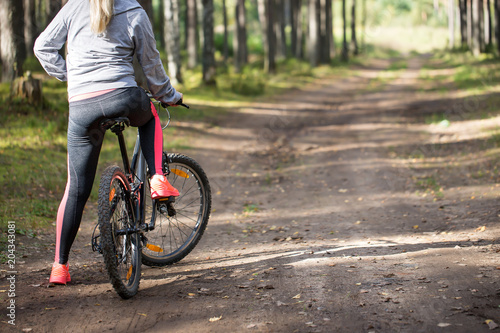 Woman riding a mountain bicycle along path at the forest © photopixel