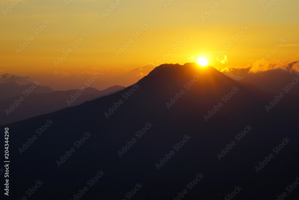Landscape of silhouette mountains at sunrise with orange skies.