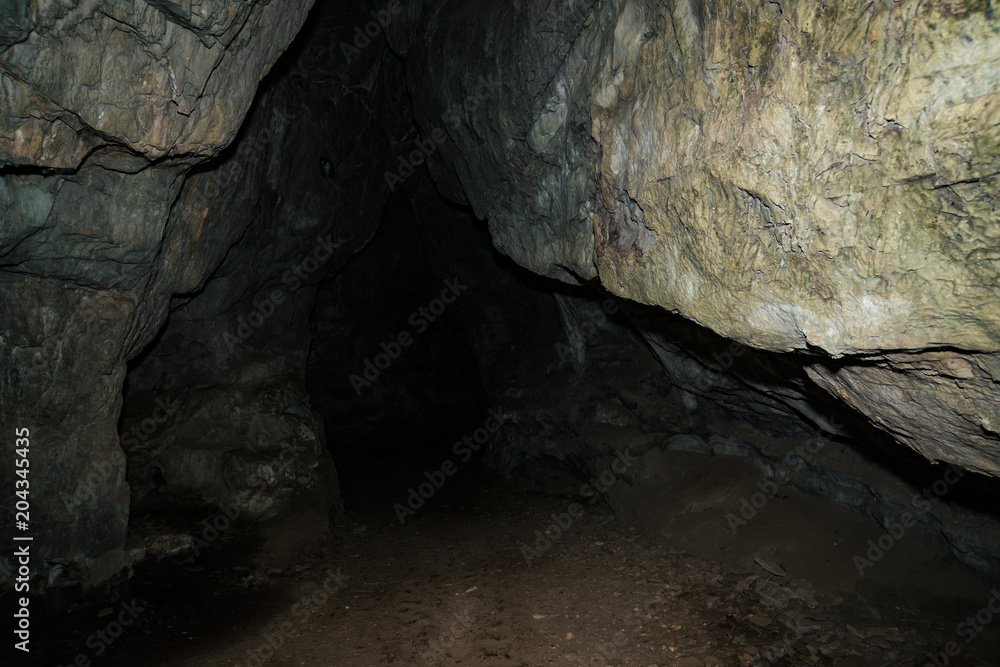 Beautiful cave. View from inside dark dungeon. Textured walls of cave. Background image of underground tunnel. Dampness inside cave. Light at end of tunnel.