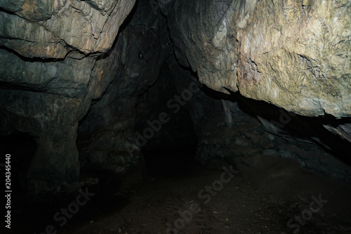 Beautiful cave. View from inside dark dungeon. Textured walls of cave. Background image of underground tunnel. Dampness inside cave. Light at end of tunnel.