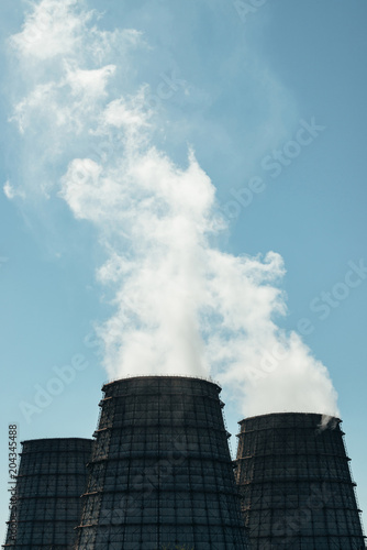 Two big tower of CHPP close-up. White steam from wide pipe of CHP on blue sky. Industrial background image of TPP with copy space. Huge pipes of thermal power plant produce steam for electric power.