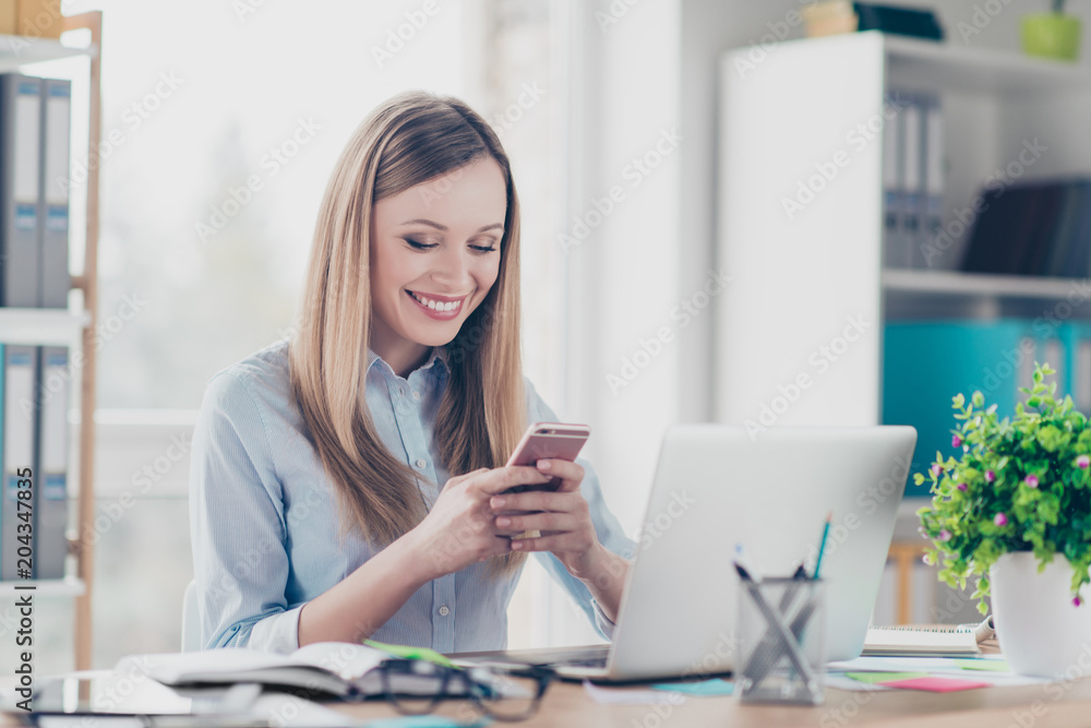 Portrait of cheerful, positive, stylish woman having smart phone in arms, checking email, using wifi, 3G internet, chatting with friends, sitting in work place, station at desktop Portrait of cheerful, positive, stylish woman having smart phone in arms, checking email, using wifi, 3G internet, chatting with friends, sitting in work place, station at desktop