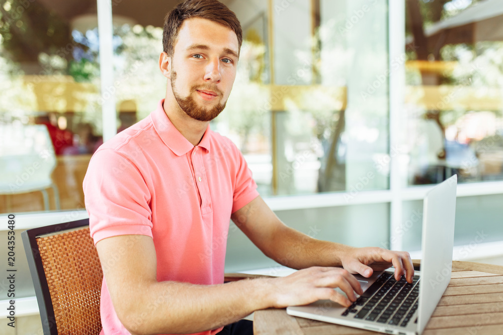 a young man sits in a cafe on the street, outdoors with a laptop a young man sits in a cafe on the street, outdoors with a laptop