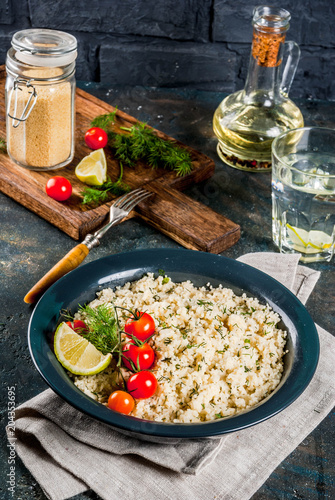 Light dietary food, couscous with tomatoes, lime and fresh herbs in dark bowl, dark blue background copy space