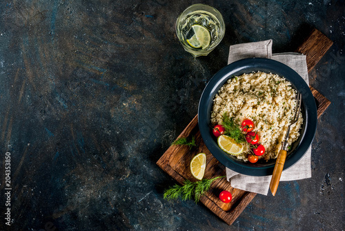 Light dietary food, couscous with tomatoes, lime and fresh herbs in dark bowl, dark blue background copy space