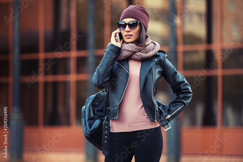 Young fashion woman in black leather jacket using cell phone in city street © Wrangler