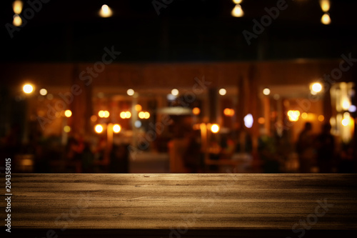 Image of wooden table in front of abstract blurred restaurant lights background.