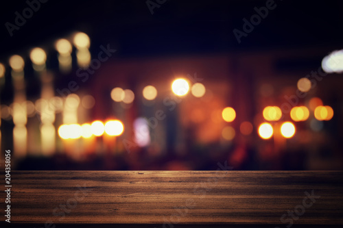 Image of wooden table in front of abstract blurred restaurant lights background. © tomertu