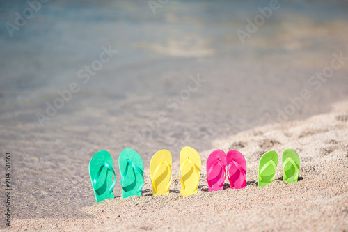 Family colorful flip flops on beach in front of the sea