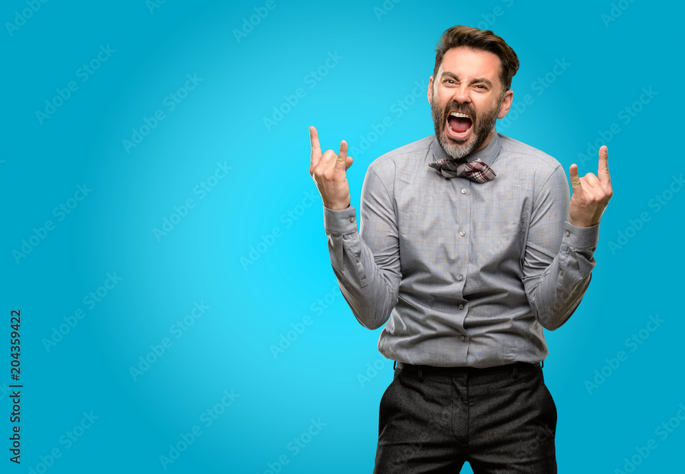 Middle age man, with beard and bow tie making rock symbol with hands, shouting and celebrating Middle age man, with beard and bow tie making rock symbol with hands, shouting and celebrating