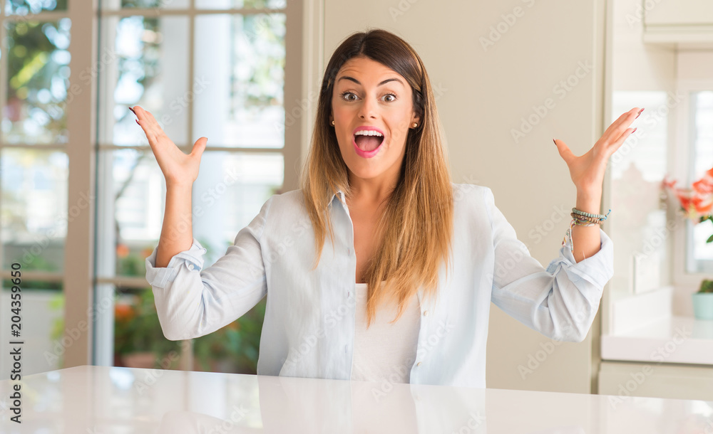 Young beautiful woman at home happy and surprised cheering expressing wow gesture Young beautiful woman at home happy and surprised cheering expressing wow gesture