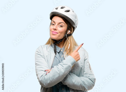 Young woman with bike helmet and earphones pointing away side with finger