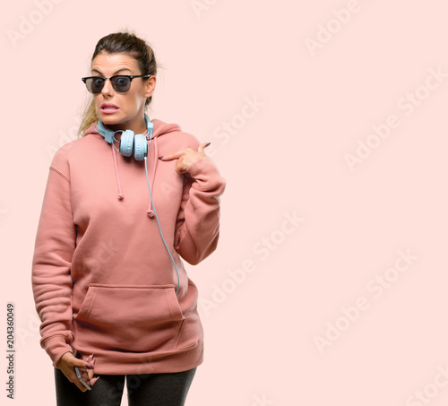 Young sport woman with headphones and sunglasses scared in shock, expressing panic and fear