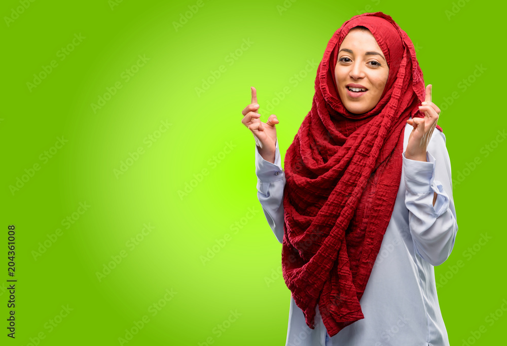 Young arab woman wearing hijab with crossed fingers asking for good luck Young arab woman wearing hijab with crossed fingers asking for good luck