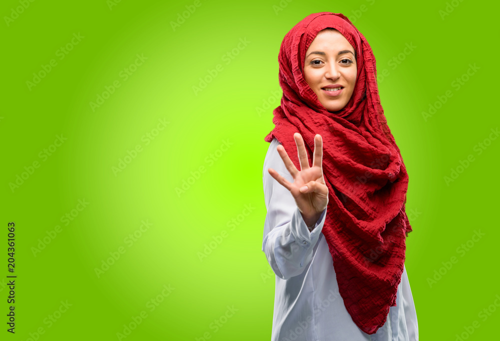Young arab woman wearing hijab raising his finger, is the number four Young arab woman wearing hijab raising his finger, is the number four