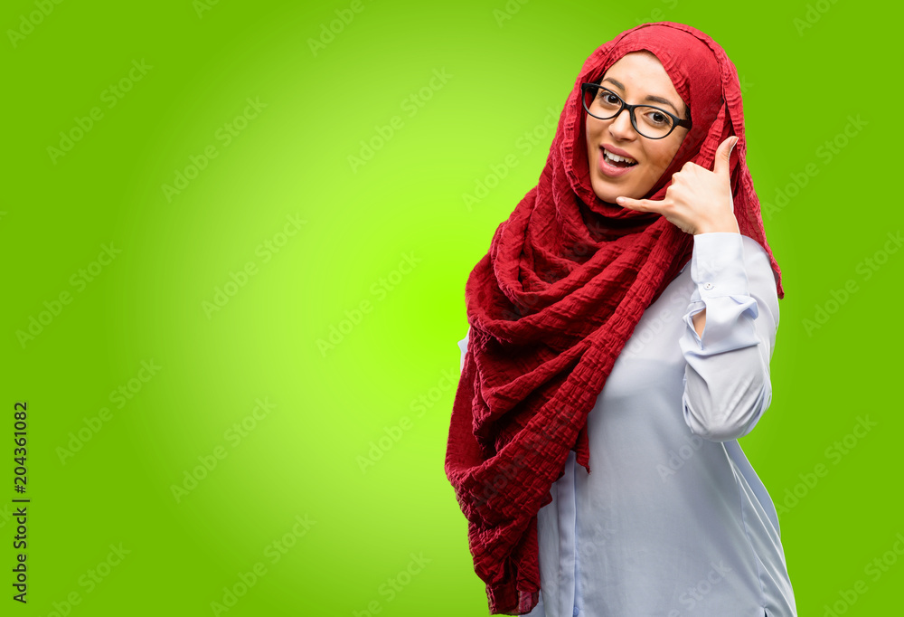 Young arab woman wearing hijab happy and excited making showing call me gesture with hand shaped like telephone Young arab woman wearing hijab happy and excited making showing call me gesture with hand shaped like telephone