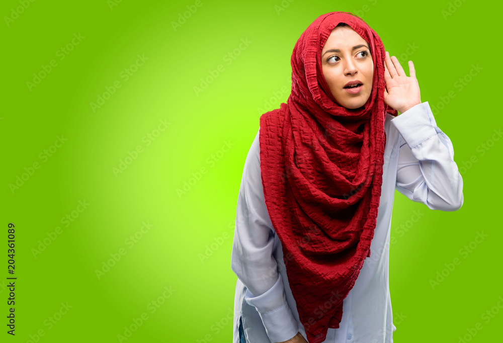 Young arab woman wearing hijab holding hand near ear trying to listen to interesting news expressing communication concept and gossip Young arab woman wearing hijab holding hand near ear trying to listen to interesting news expressing communication concept and gossip